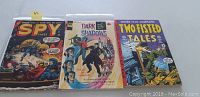 Front view of three vintage comic books: Spy Cases #17, Dark Shadows #27, and Two-Fisted Tales Annual #4 placed side by side showing colorful cover art and titles.
