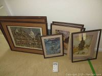 Grouped framed art prints and paintings leaning against a white wall, showing different sizes and styles including cityscape and abstract themes.