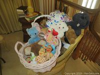 Photo showing a collection of various stuffed animals in two white woven baskets, placed on a chair next to a staircase.