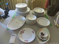 Full view of various stacked china dishes and plates including floral patterned and golden wheat motif plates