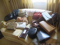 A collection of vintage handbags and purses displayed on a couch, showing various colors and styles, including leather and fabric materials.