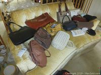 View of 15 plus vintage handbags displayed on yellow sofa, showing variety of colors and materials