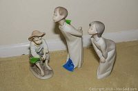 Three Lladro figurines side by side showing scale and condition, two standing and one seated boy figurine.