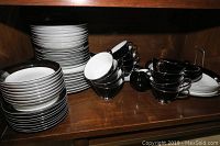Photo of stacked white plates and black tea cups showing the dinnerware's shape and color.