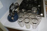 Twelve clear glass drinking glasses with metallic rims in front of two tea kettles on stove
