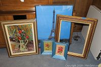 Shows five art pieces arranged on floor: floral print, Eiffel Tower poster, two small framed embroidered flowers, and an empty frame
