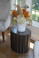 Side table with vase and dried flowers, showing scalloped metal edge and scuffs on surface