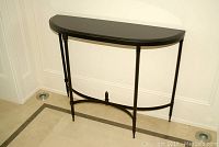 Front angle view showing the entire demilune table against the wall on a tiled floor.