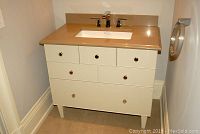 Front view of white painted vanity with six drawers, brown Caesar stone top with backsplash, chrome knobs, and sink with faucet.