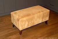 Three angled views of the beige suede-like upholstered rectangular bench ottoman with dark wooden legs showing wear.