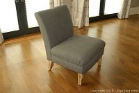Gray upholstered chair with nailhead trim and distressed wooden legs, shown from a right-side angle on hardwood floor.