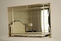 Front view of the large rectangular mirror mounted on a wall reflecting furniture and window.