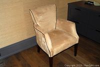 Front-left angle view of the camel microsuede armchair with black piping, showing overall shape and legs.
