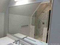 Full view of large rectangular wall mirror above bathroom counter, showing metal frame and reflective surface.