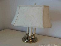 Full view of the lamp showing the rectangular fabric shade and brass base with candle-style holders.