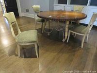 Overview of four dining chairs around a circular wooden dining table, showing distressed cream-colored frames and light upholstery.