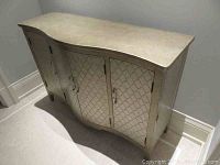 Front view showing curved top and three-door front with silver lacquer finish and lattice-pattern inlay