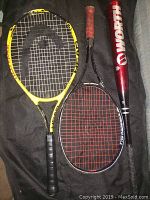 Photo showing a red Worth softball bat next to a black Dunlop Ferrex tennis racket and a yellow HEAD tennis racket on a black carry bag.