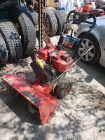Red Craftsman 25-inch snowblower viewed from front angle showing engine, wheels, and handle bars with tires in background.