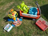 Photo shows a red and white kid’s wagon with green frog seat insert, blue Bumbo baby chair, multicolored animal activity toy, assortment of dolls, children’s picnic set, and white and red hamster cage.