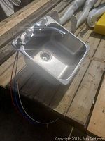 Stainless steel sink with attached faucet and hot/cold water handles placed on wooden surface.