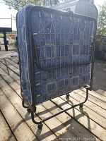 Folded view of the metal frame and mattress of the foldable single bed showing wheels and support structure