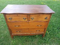 Front view of wooden dresser showing four drawers with metal handles and key holes, scalloped top edge, and wood grain finish.