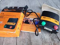 Photo showing Gallagher M20 Yardmaster electric fence energizer with original box and user manual on wooden surface.