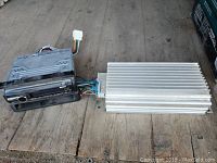 Sony car stereo deck and Bose amplifier side by side on wood floor, front view of deck and side view of amplifier showing wiring and heat fins.