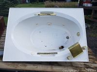 Top view of white oval Jacuzzi bathtub showing interior, brass faucet fixtures, and jet nozzles. Multiple pitted spots and signs of wear visible on surface.
