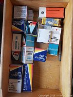Top-down view of a wooden drawer containing 13 boxed projector bulbs from various brands, all in vintage packaging with colorful labels.