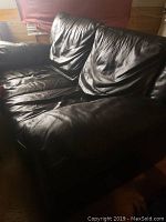 Front angle view of the black full grain leather loveseat with visible seat and back cushions showing natural leather creasing.