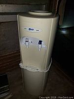 Front view of beige Super water cooler dispenser with two taps and drip tray.