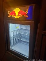 Front view of bar fridge showing illuminated Red Bull logo header, glass door and interior shelves