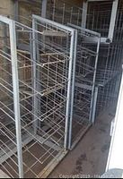 Two large industrial rolling racks made of steel with multiple horizontal wire shelves and heavy castors, shown in a storage area.