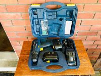 Blue molded plastic carrying case open on wooden surface with Mastercraft cordless drill, two batteries, charger, and small parts compartment inside.