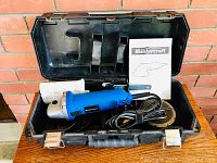Open black plastic carrying case holding Mastercraft electric angle grinder with power cord, grinding disc, and included documentation and accessories.
