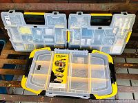 Three Stanley plastic organizers with transparent lids showing compartments of screws, bolts, nuts, washers, and wall anchors.