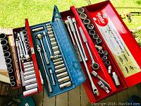 Photo showing three red Husky metal toolboxes with assorted socket sets and ratchets displayed open on a porch railing.