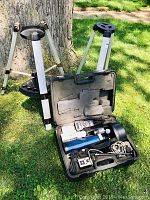Two aluminum adjustable tripods and open hard case showing telescope components