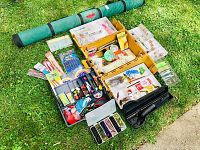 Full lot spread out on grass showing green rod tube, two large yellow tackle boxes filled with lures and fishing gear, small lure boxes and accessories, and black hard plastic rod case.