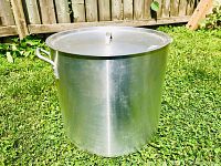 Full view of large aluminum stock pot with lid on top outdoors on grass.