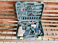 Wide view of open green plastic molded case showing all tools and accessories inside against brick backdrop.