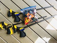 Four Quick-Grip clamps arranged on floor with large plastic bag filled with many smaller clamps in orange, blue, and black colors.