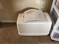 White hard plastic sewing basket case with handle, manual on top.