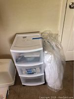Full view of the three-drawer plastic tote with a pillow wrapped in plastic beside it.