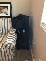 Photo showing the small black wood side table next to a striped sofa with one wood storage basket on the table.