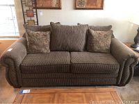 Front view of the overstuffed brown upholstered sofa with decorative cushions arranged on seating.