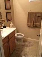 View of bathroom with toilet, vanity, brown towels on towel rack, oval bath rug, and two framed wall art pieces on wall