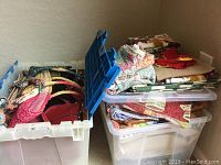 Two plastic storage bins with assorted table cloths and towels inside, top bin lid open showing contents